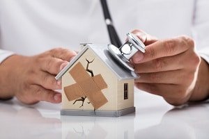 House with a stethoscope being applied to it by a doctor